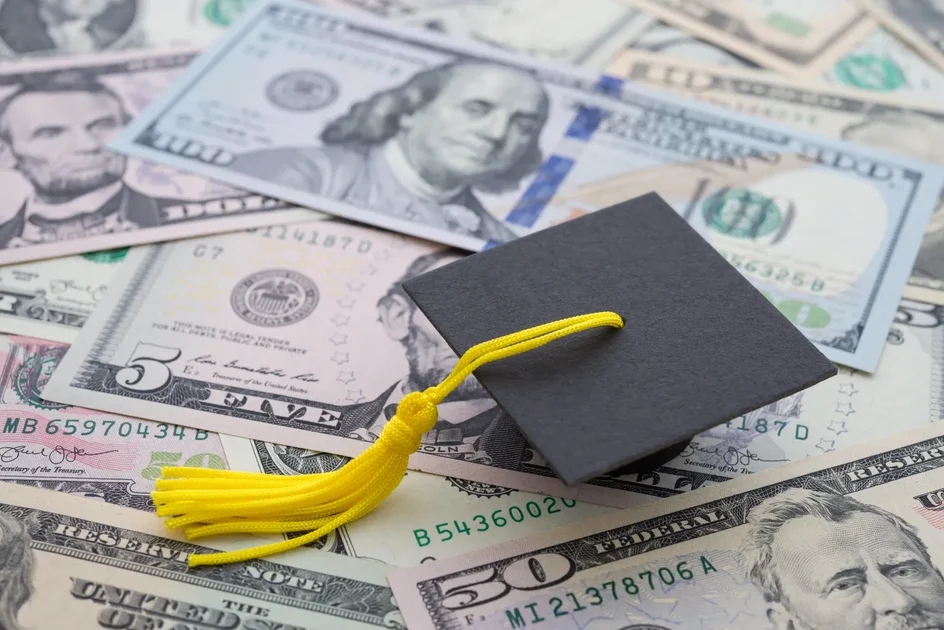 Stock image of a graduation cap on a background of U.S. currency.