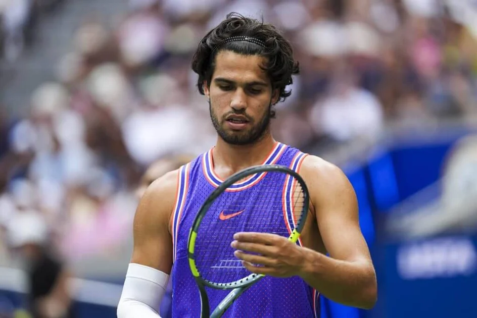 Carlos Alcaraz looks down at his tennis racket.