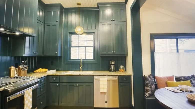 Wood paneled small kitchen with deep green cabinets and paneled walls.